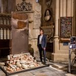 A man stands looking at an art installation of a bomb damaged door from Ukraine, located in the chapel of a church with a prayer wall behind him.