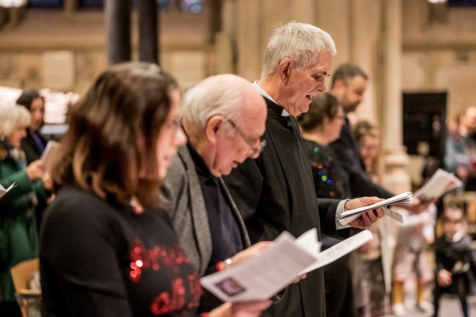 A member of the clergy and congregation sing from order of service booklets in a church