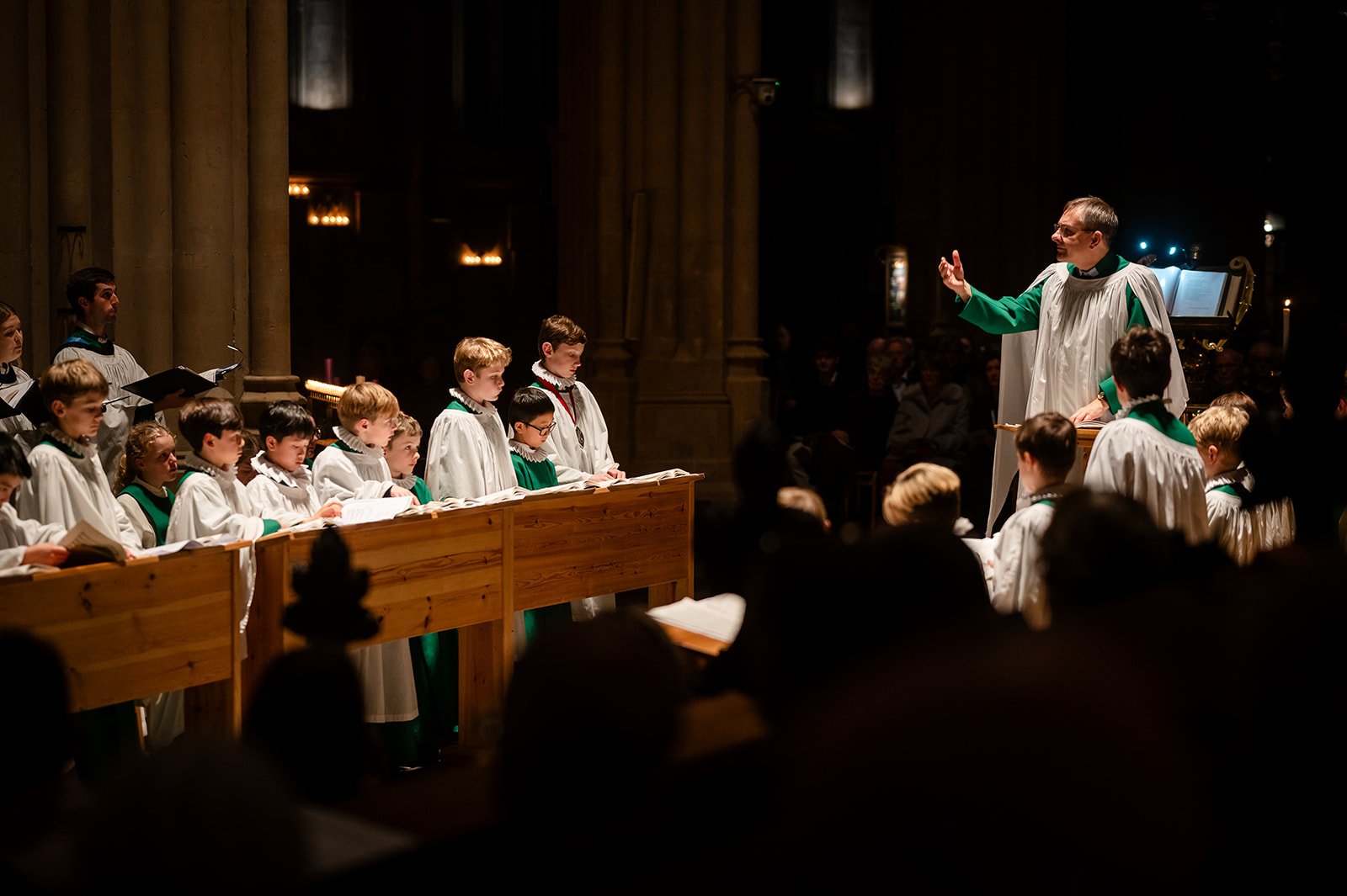 A choir master conducts a choir singing in a dark church