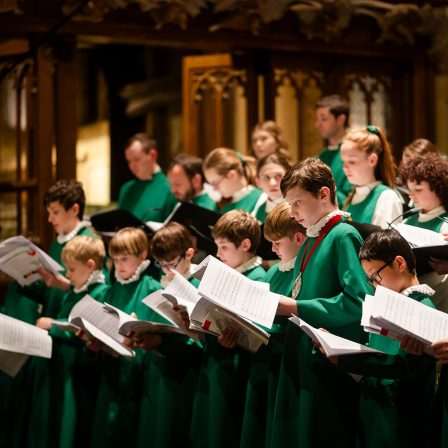 A mixed group of choristers in green robes, holding sheet music in a church