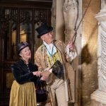 A man and woman in period Regency costumes look at a memorial on Bath Abbey's walls