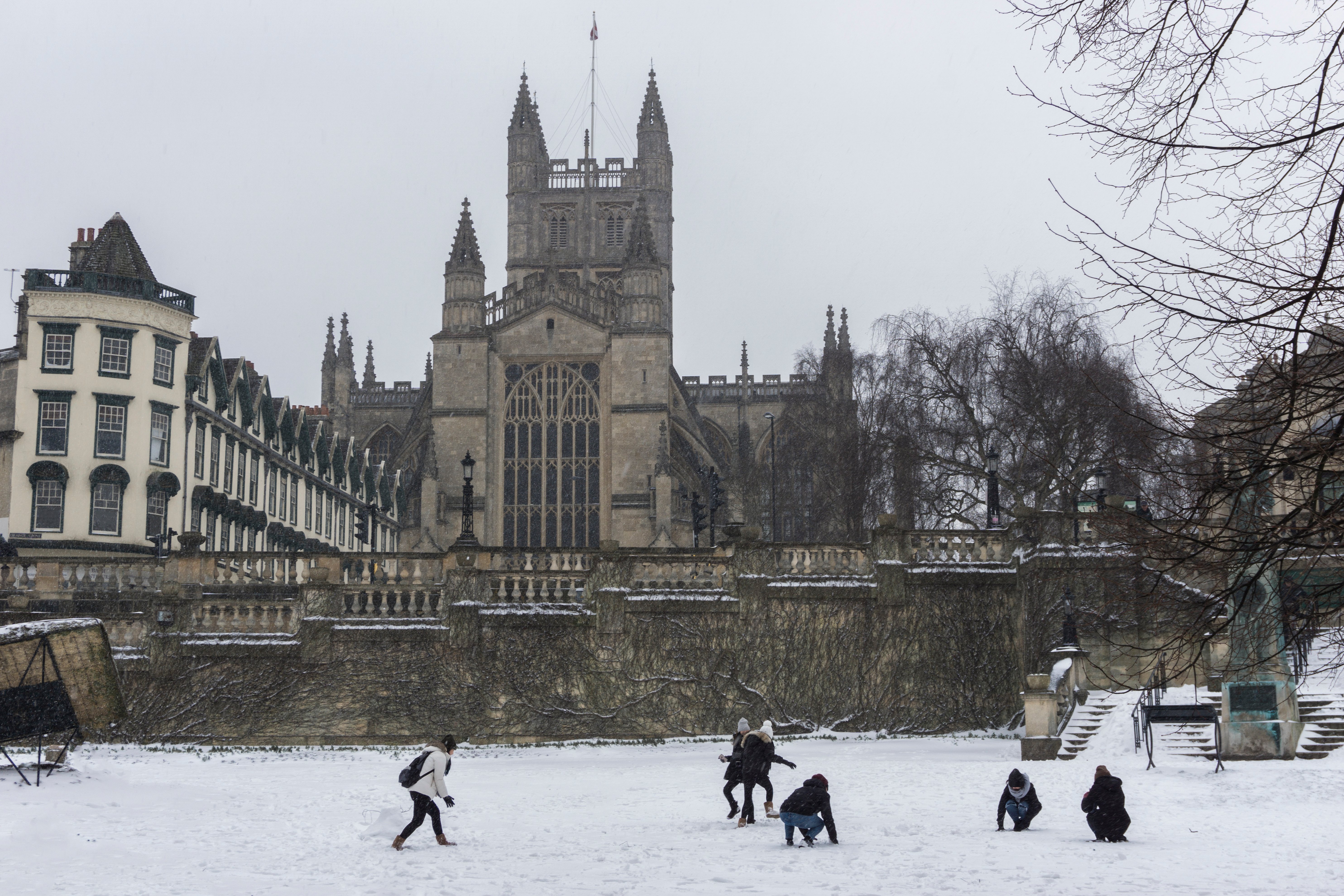 Bath Abbey shown from Parade Gardens, with people playing in the snow